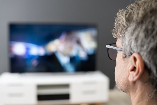 Man Watching Tv Movie Or Television In Glasses A person watches a mesothelioma commercial while thinking of their loved ones.